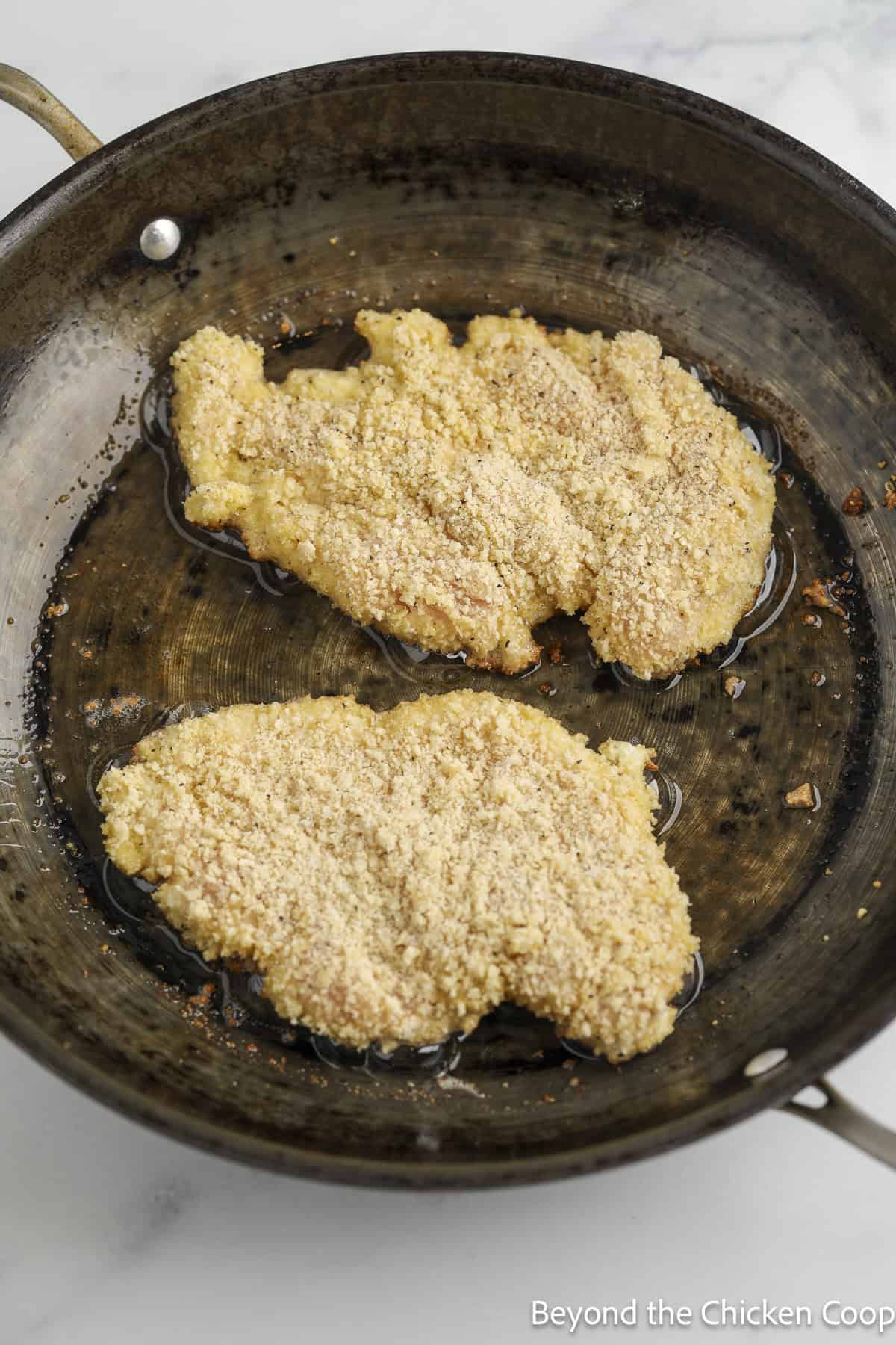 Cooking two breaded chicken breasts in a skillet.
