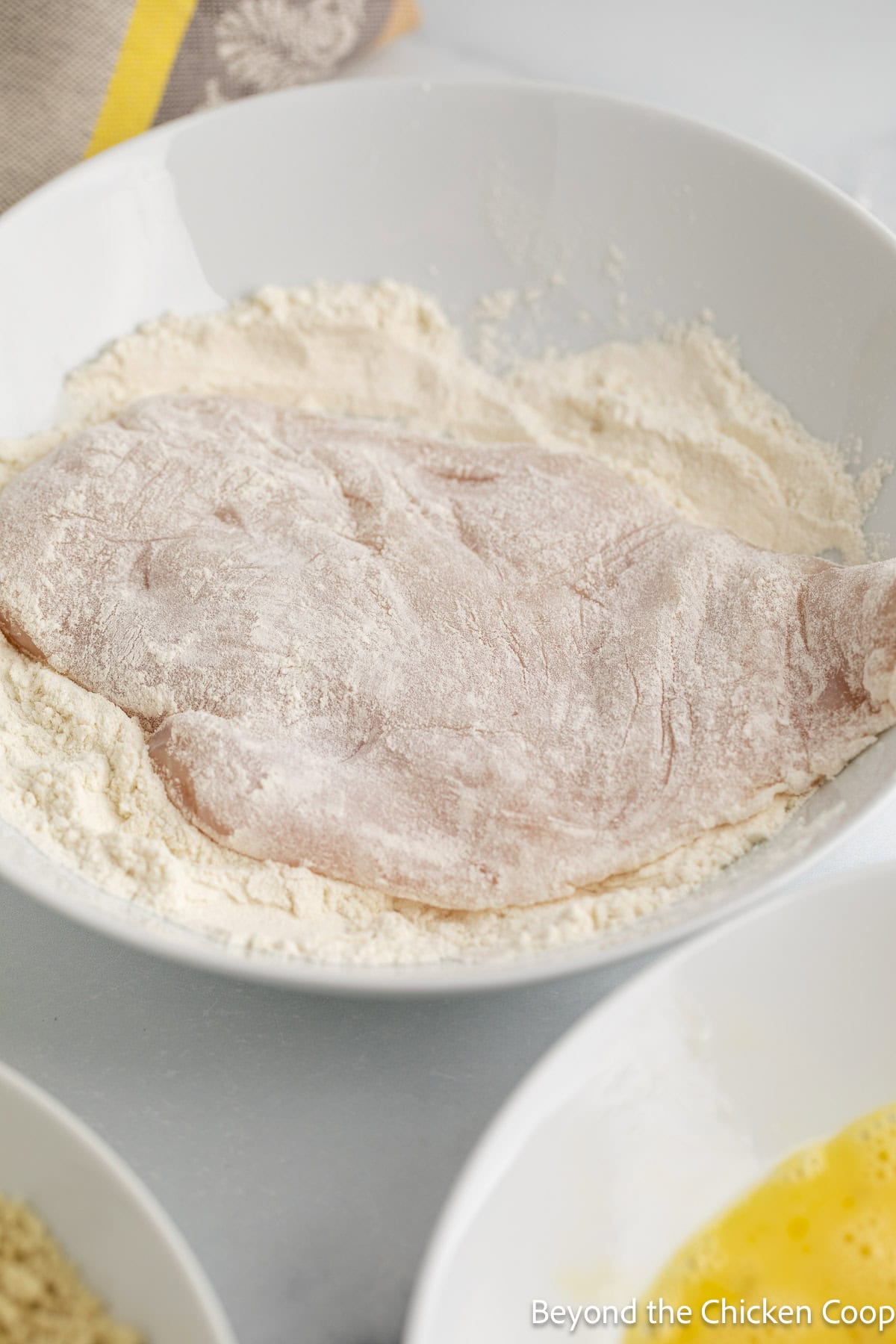 Dipping a chicken breast into flour.