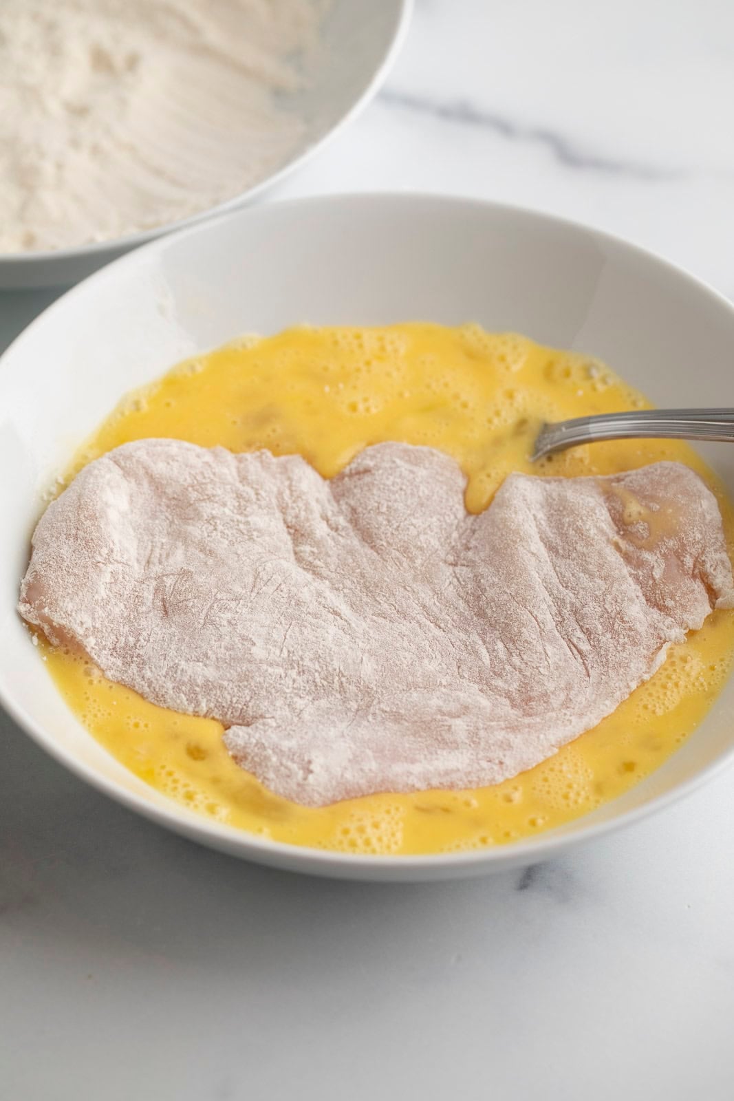 Dipping a chicken breast into beaten eggs.