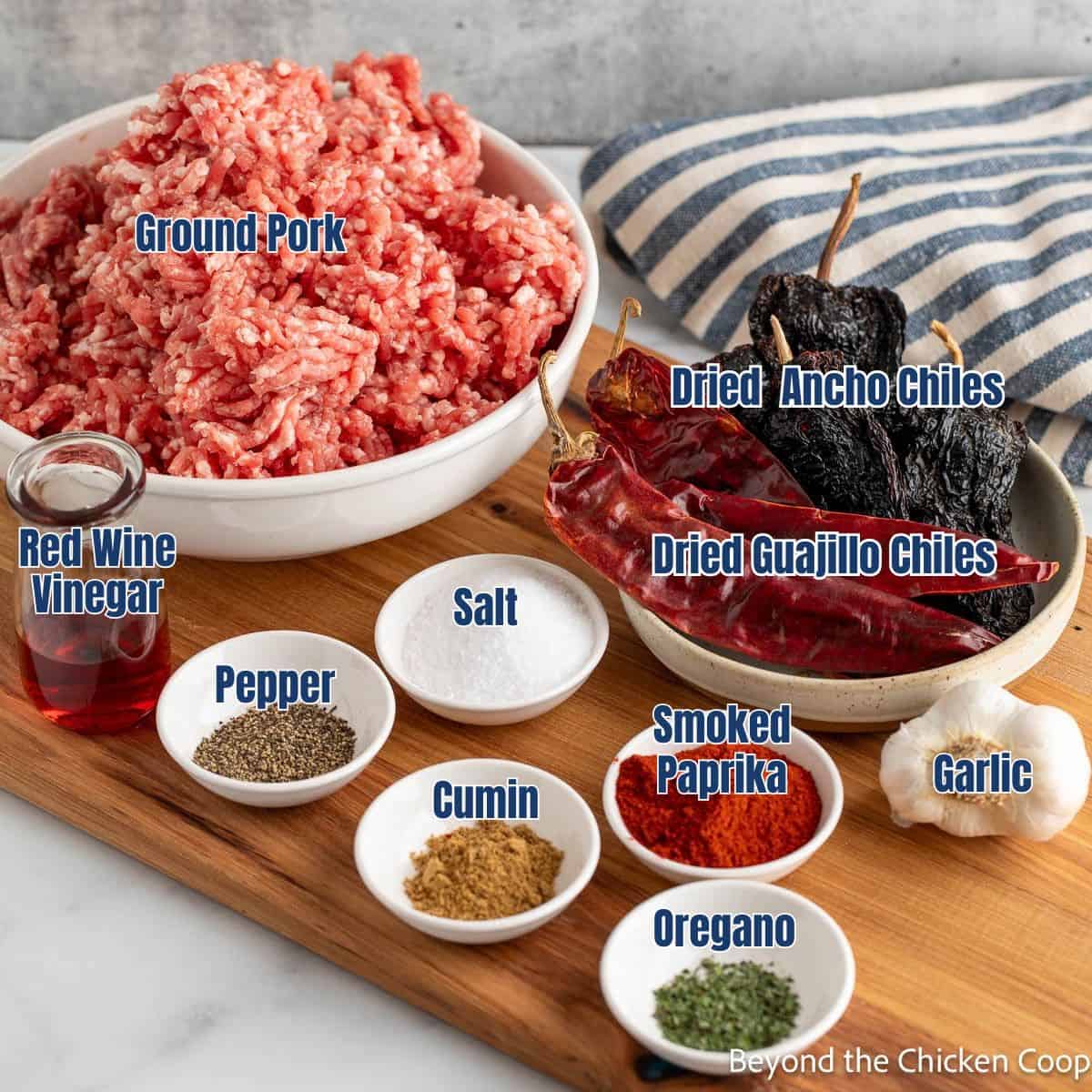 Spices in small bowls along with dried chiles and ground pork.