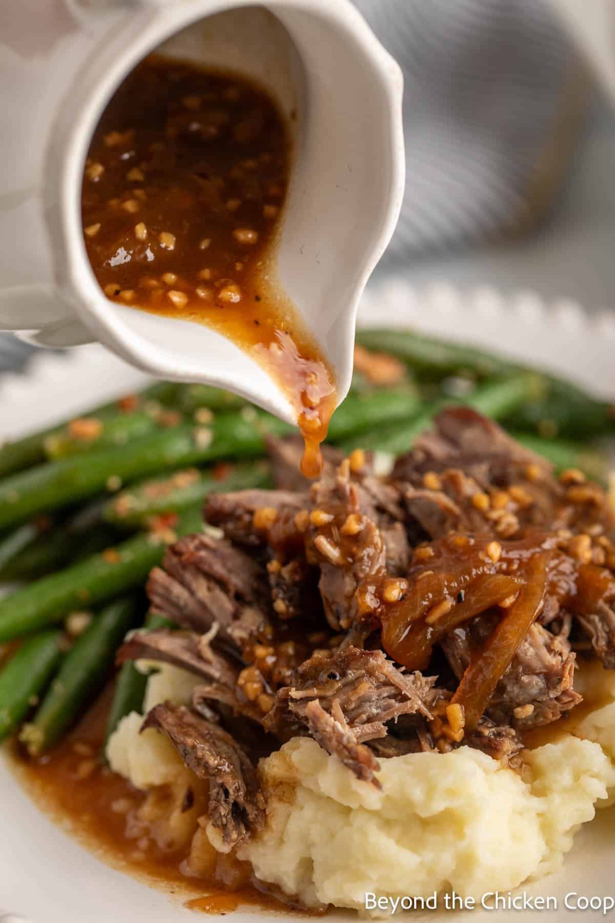 Gravy pouring over shredded beef on mashed potatoes.