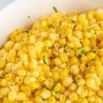 Corn kernels in a white dish topped with a bit of chopped parsley.