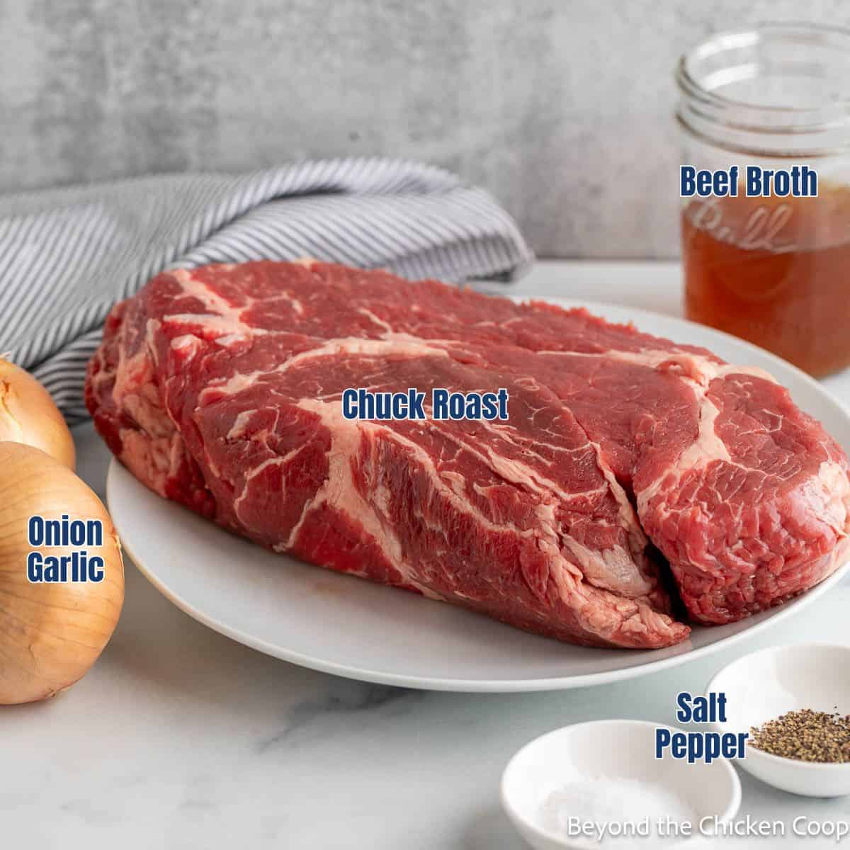 A chuck roast next to a jar with beef broth and fresh onions.