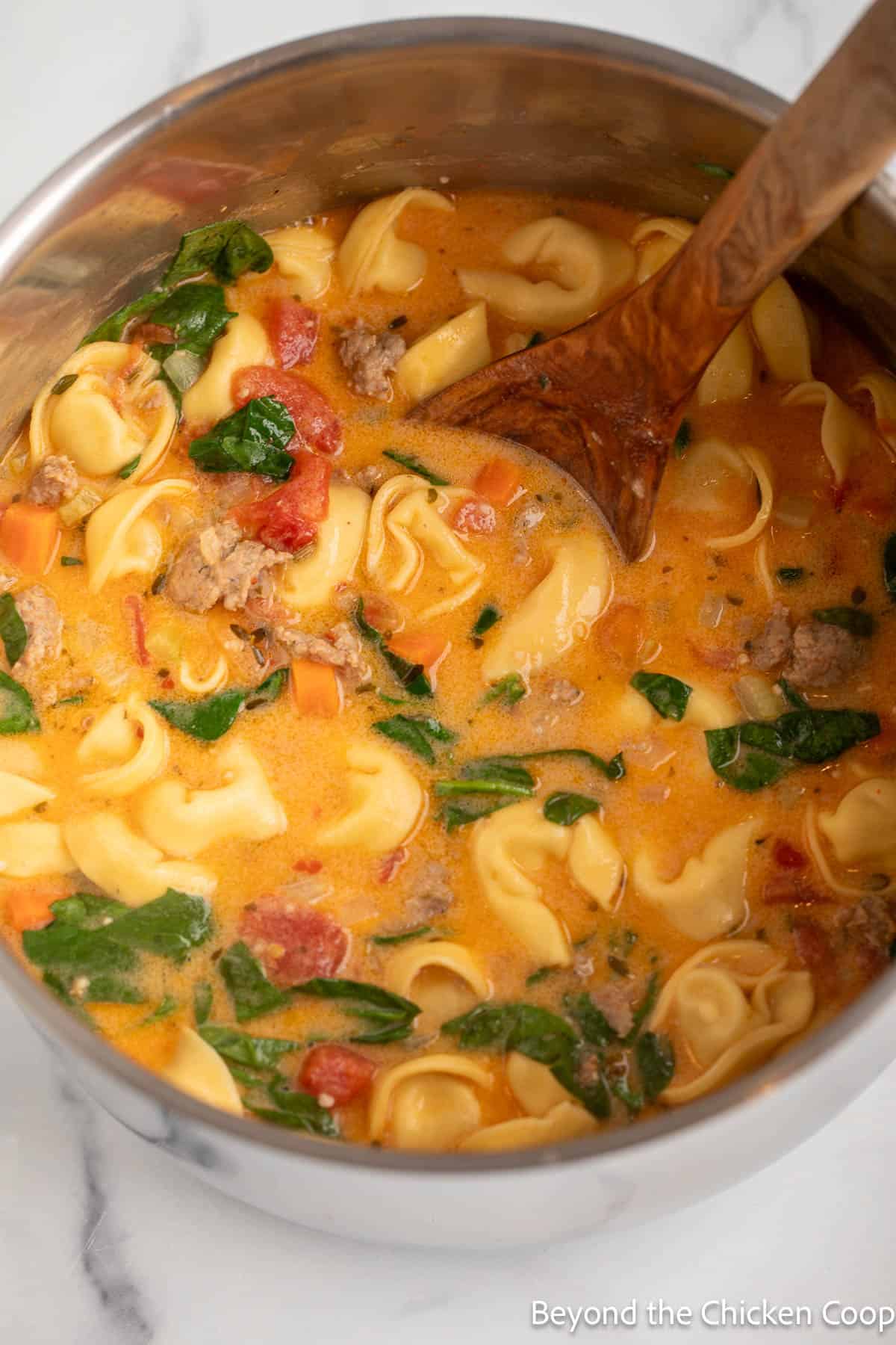 Italian sausage, spinach, and tortellinis in a pot of soup.
