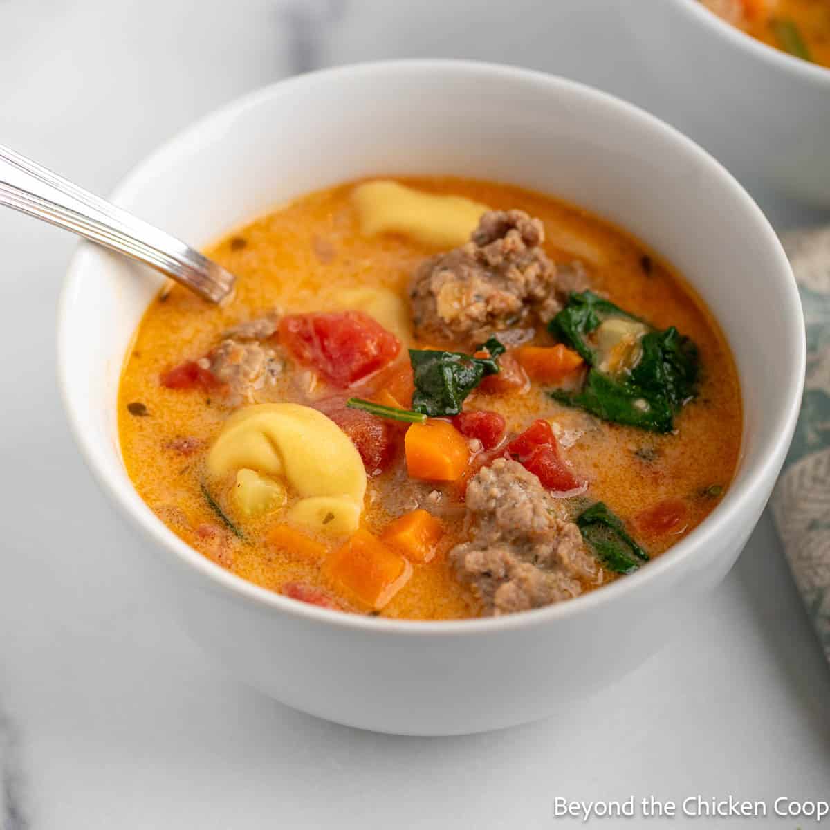 Creamy Tortellini Soup with spinach in a white bowl.
